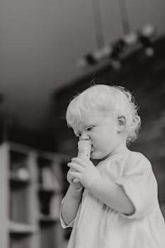 Adorable toddler in grayscale, holding an object inside a cozy home setting.