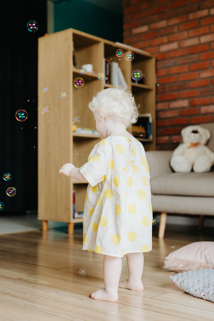 Baby In Polka Dot Dress Standing On Wooden Floor