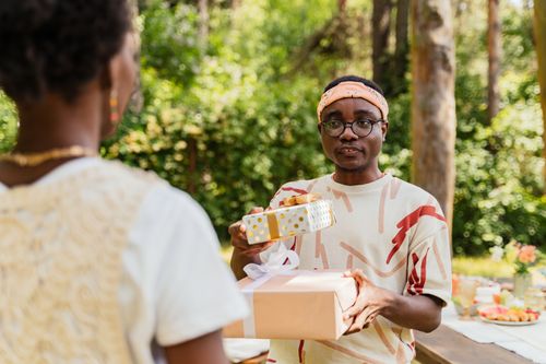 Free Two friends exchange gifts at an outdoor gathering, capturing a moment of joy and celebration. Stock Photo