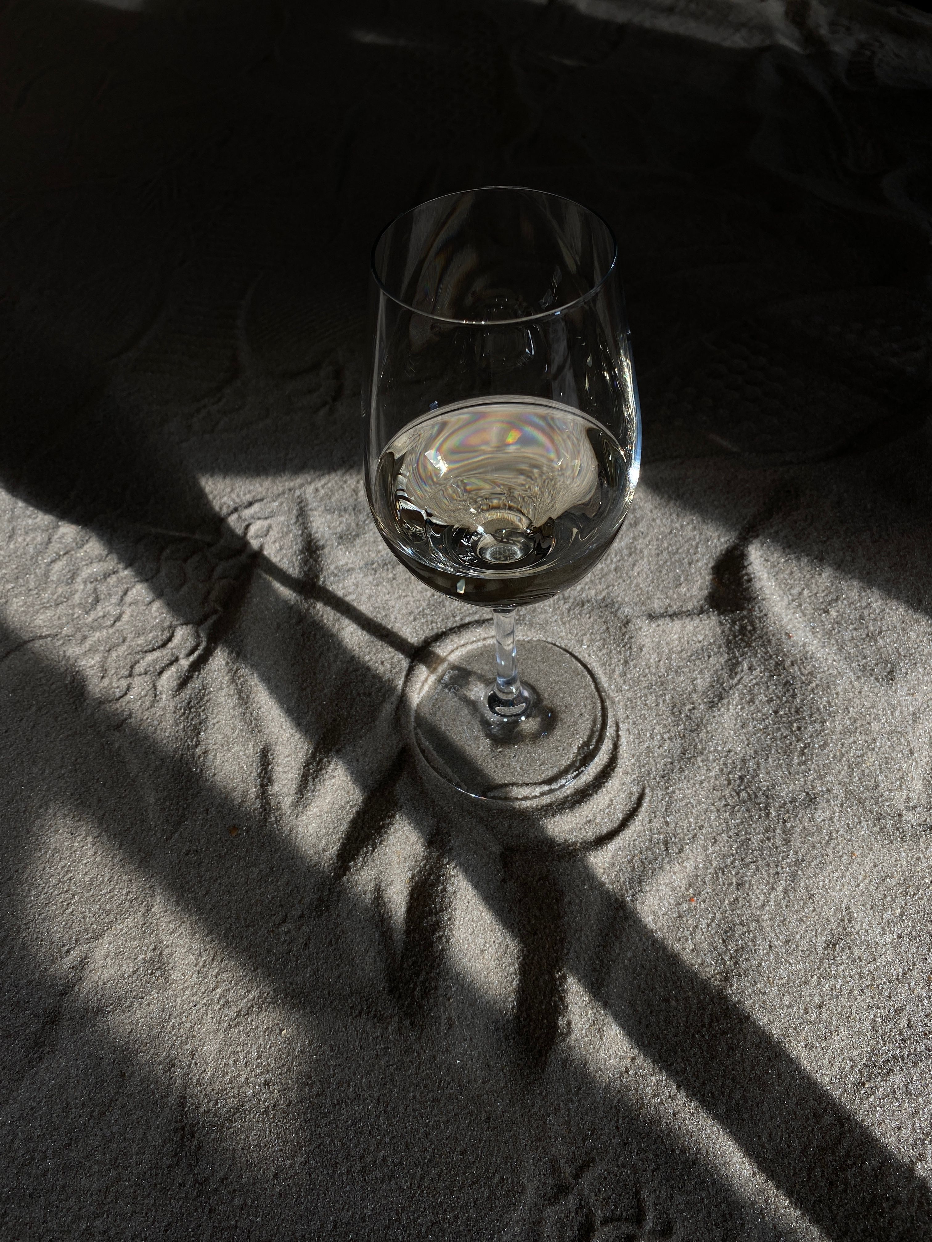Artistic shot of a wine glass casting shadows on sand, with a focused light play that offers a dramatic and intriguing scene.