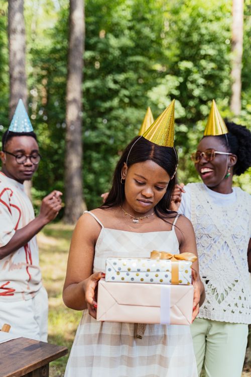 Free Friends celebrating a birthday outdoors with party hats and presents. Stock Photo
