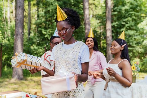 Free Four friends celebrate a birthday outdoors with party hats and gifts in a summer setting. Stock Photo