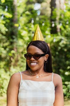 Happy woman in sunglasses and party hat outdoors, exuding joy and leisure.