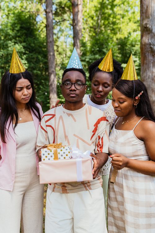 Free Friends celebrate a birthday outdoors with party hats and gifts, enjoying the festive moment. Stock Photo