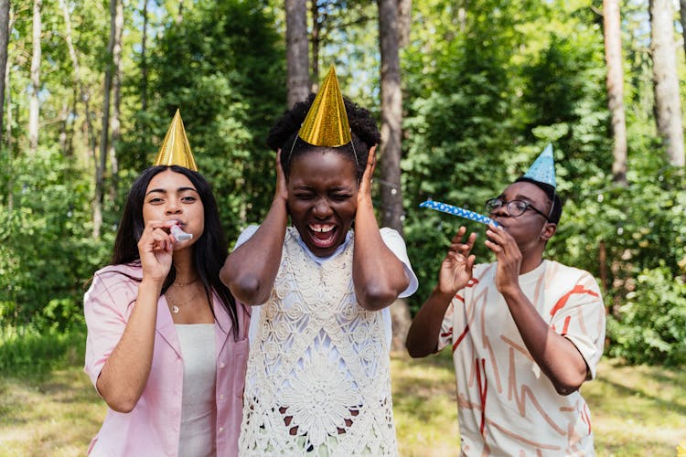 A Young Woman Covering Ears While Friends Are Blowing Party Trumpets  