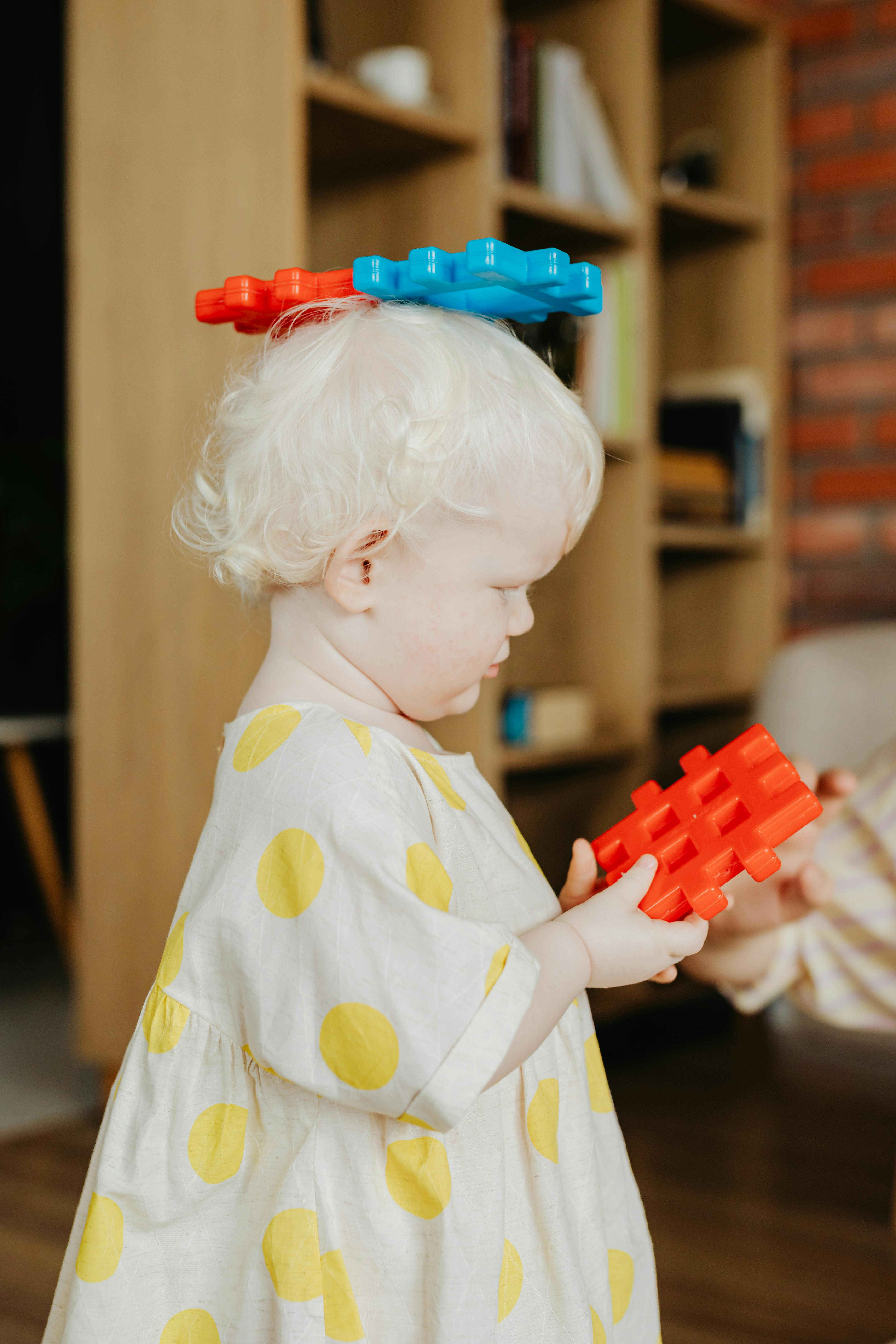 Cute young child with albino traits playing creatively with colorful building blocks indoors.