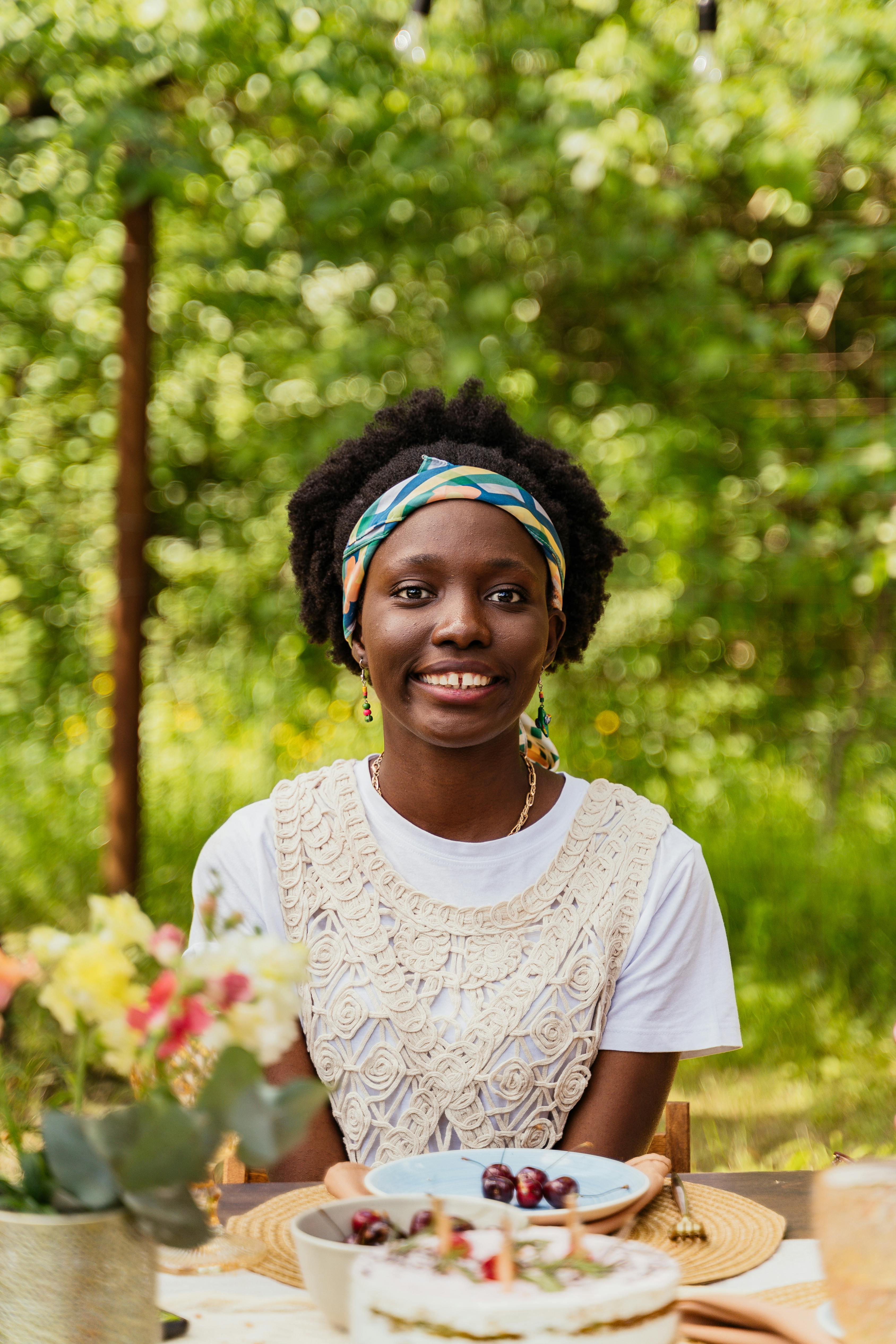 A cheerful woman sits outdoors, surrounded by nature, enjoying a relaxing picnic with food and flowers.