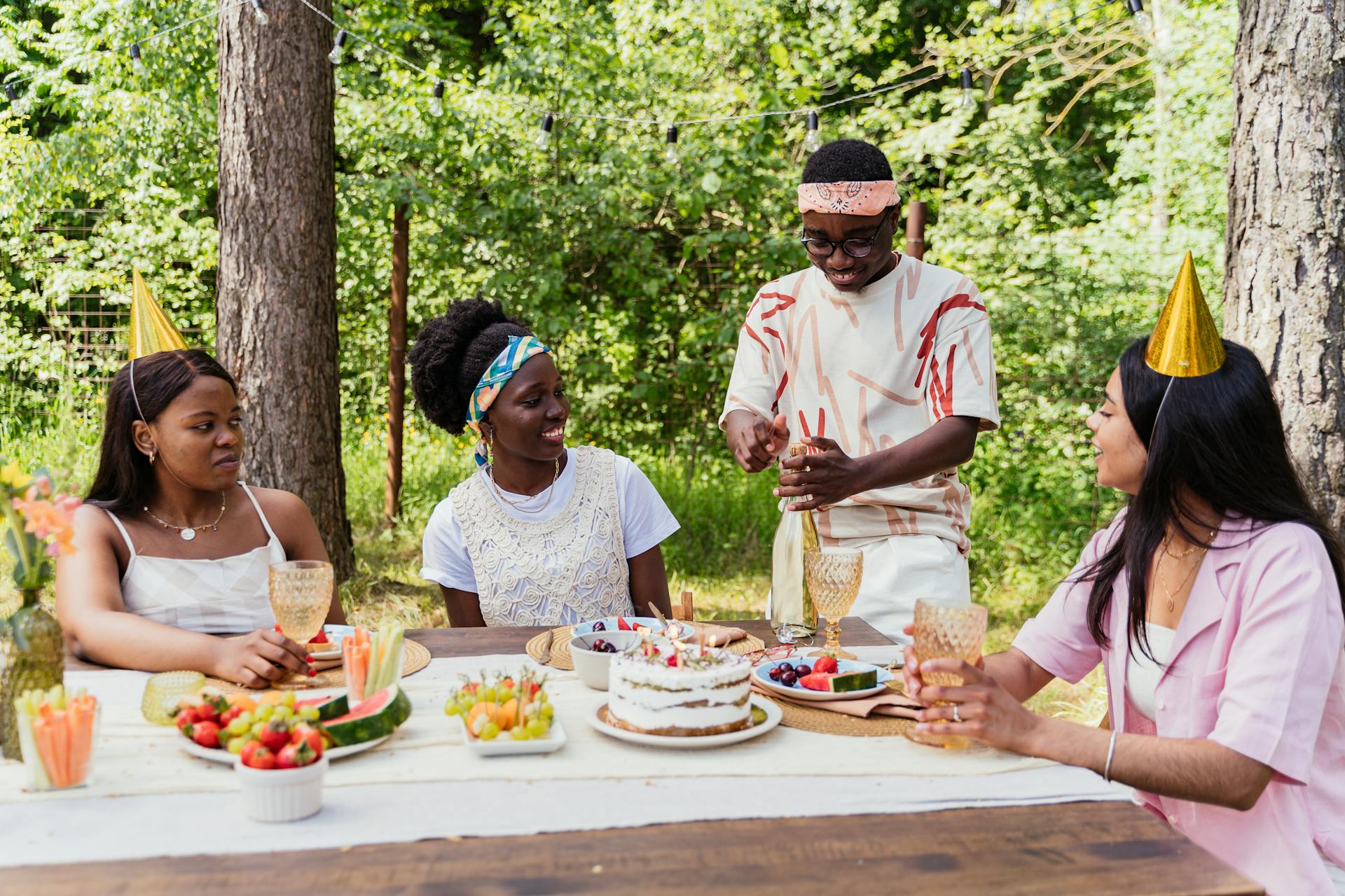 Group of friends enjoying a birthday party outdoors with food and drinks.