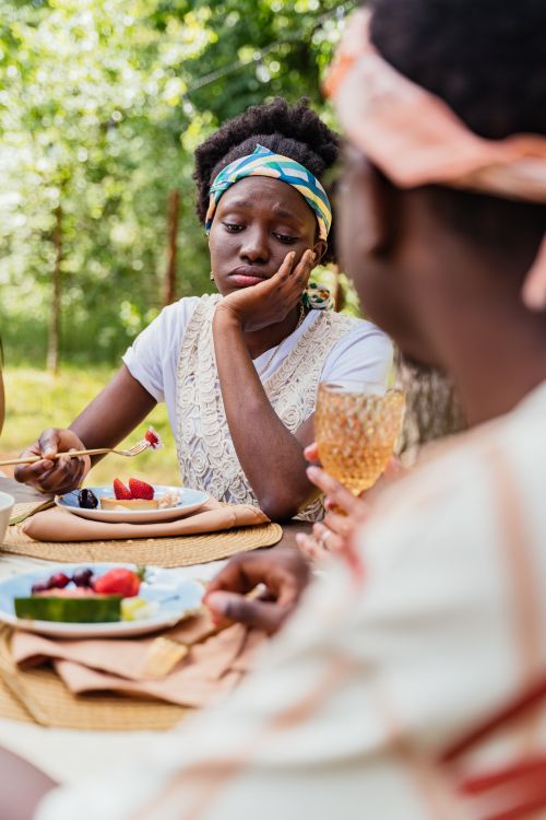 Free Woman looking contemplative outdoors, holding a fork with fruit at a picnic table. Stock Photo