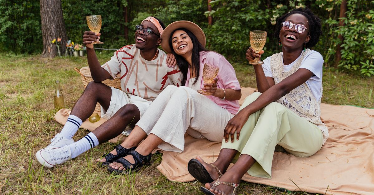 A group of diverse young people laughing while having a picnic in a sunny park, with reusable water bottles and homemade food