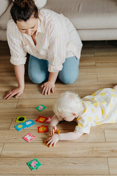 A Woman Kneeling on Floor Watching a Baby Playing with Flashcards