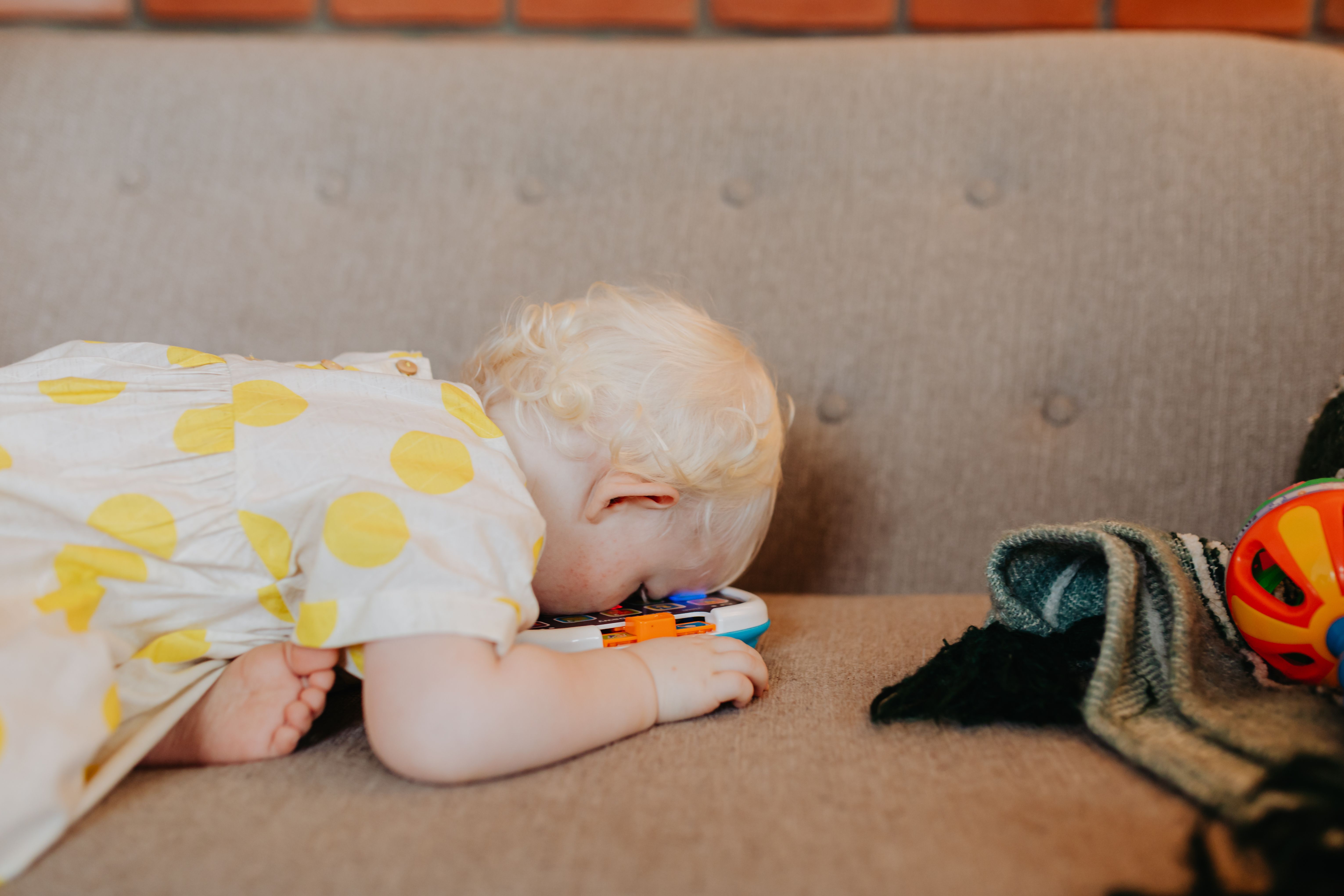 Cute baby with blonde hair playing with a toy on a cozy couch indoors.