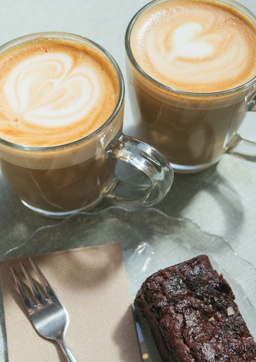 Free Two lattes with beautiful art and a brownie on a plate, perfect for coffee lovers. Stock Photo