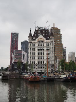 Historic White House in Rotterdam with boats in the harbor during a cloudy day.