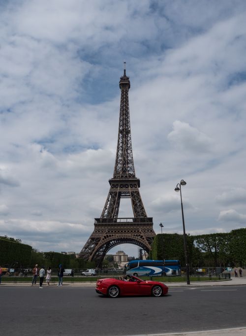 Free The Eiffel Tower stands tall with a red sports car in the foreground, capturing the essence of Paris. Stock Photo