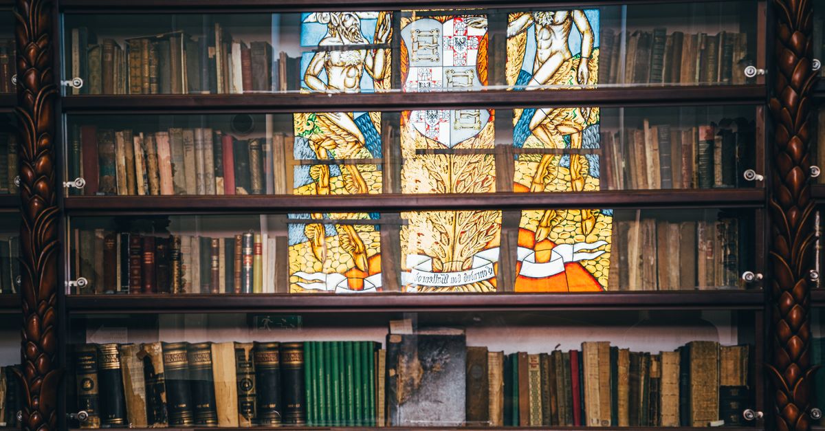 A vintage bookshelf with an ornate stained glass window reflecting vibrant colors.