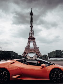 Stunning view of the Eiffel Tower with an orange luxury car in the foreground on a cloudy day.