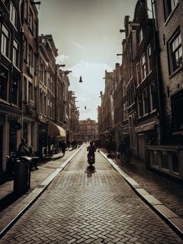 Sunlit historic street in Amsterdam with a silhouette of a scooter against classic European architecture.