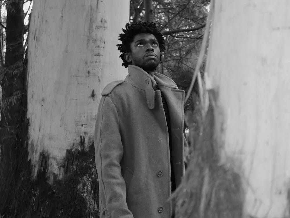 Grayscale Photo of a Man in a Trench Coat Looking Up