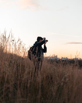 A man takes photos at sunrise in a grassy field overlooking Melbourne skyline.