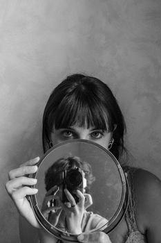Black and white portrait of a woman holding a mirror, capturing her reflection.