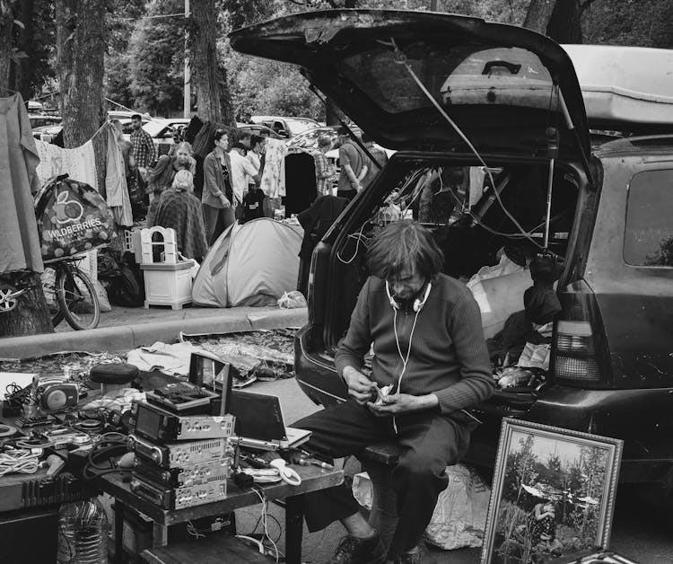 Grayscale Photo Of A Man On The Back Of A Car Selling Electronics