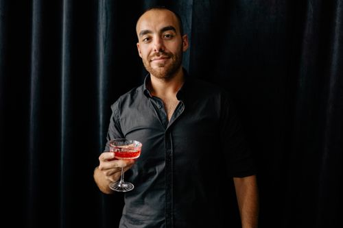 Free A sophisticated man in a button-up shirt holds a crystal glass of wine against a dark background. Stock Photo