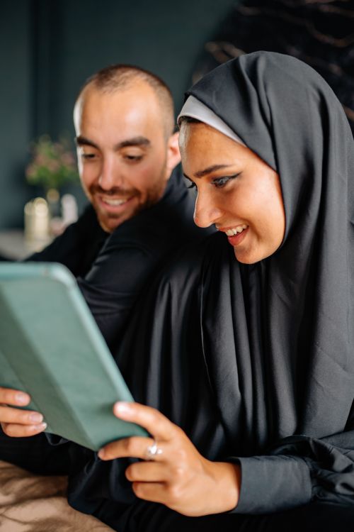 Free Muslim couple happily using tablet together indoors, sharing a joyful moment. Stock Photo