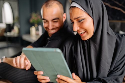 Free Woman in Black Hijab Holding Ipad Beside Man in Black Robe Stock Photo