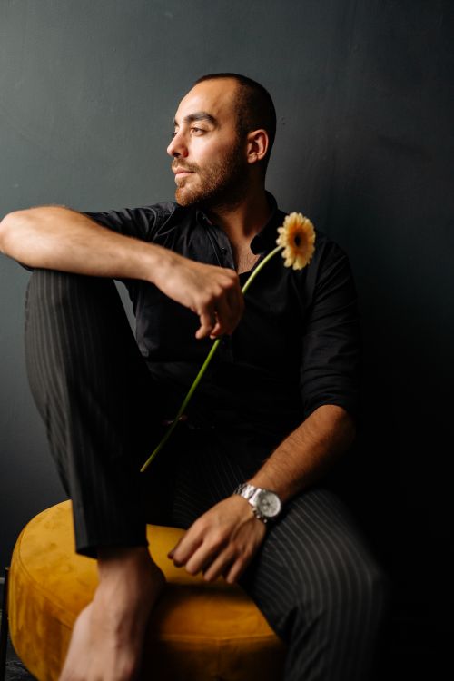 Free A man in a dark room looking sideways, holding a flower, seated with a thoughtful expression. Stock Photo