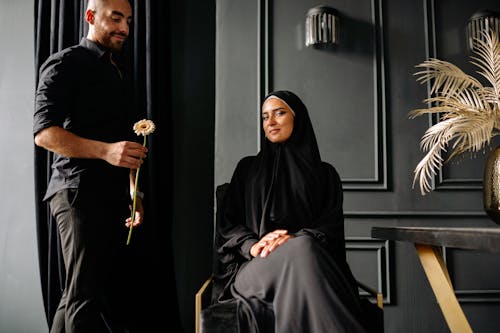 A Man Standing Holding a Flower Besides a Woman