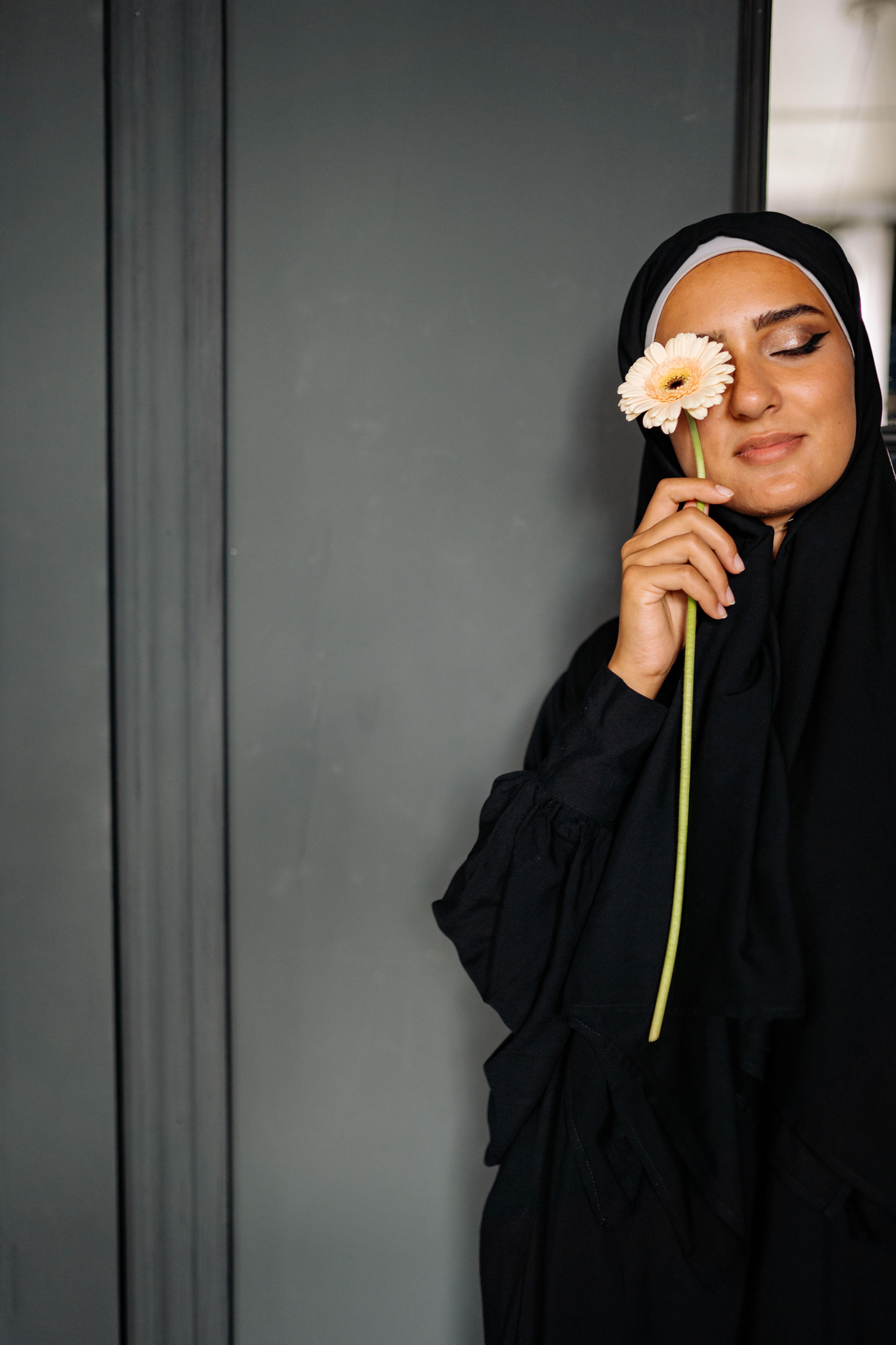 A serene portrait of a woman in a hijab holding a flower, exuding elegance and peace.