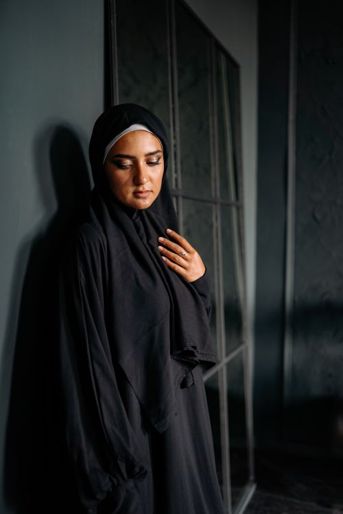 Free Portrait of a woman in a black hijab standing indoors, showcasing cultural elegance. Stock Photo