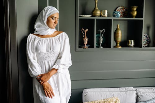 A Woman in White Hijab Standing Beside Black Wooden Cabinet