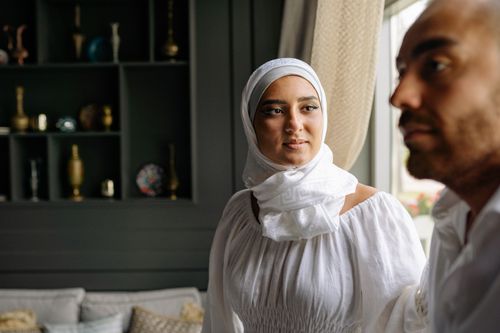 Free A young man and woman in modest attire sitting indoors, blending tradition with a modern interior setting. Stock Photo