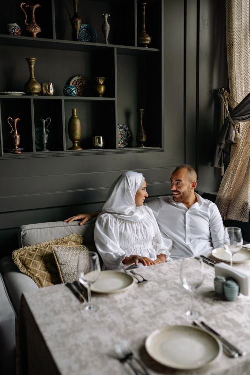 Free A couple in elegant attire sitting together on a sofa, smiling and sharing a moment. Stock Photo