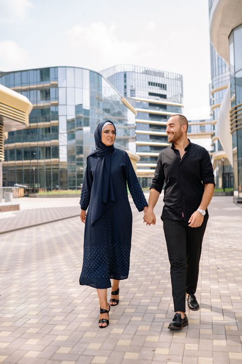 Free Smiling Muslim couple holding hands and walking on a city pavement with modern architecture around. Stock Photo