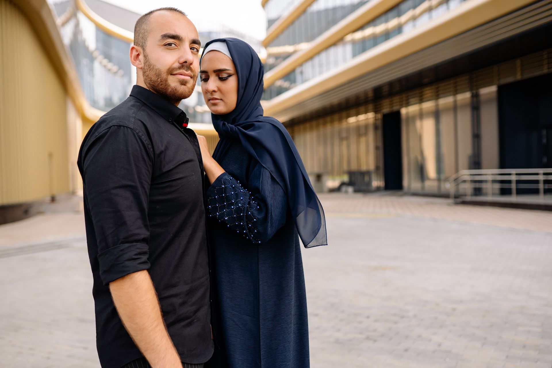 A fashionable couple poses affectionately in a sleek urban environment, showcasing modern relationship dynamics.