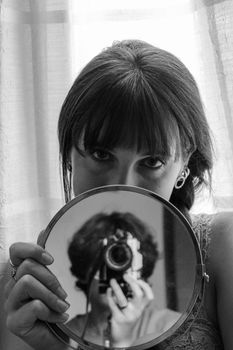 Creative self-portrait in grayscale featuring a woman with an analog camera in a mirror reflection.