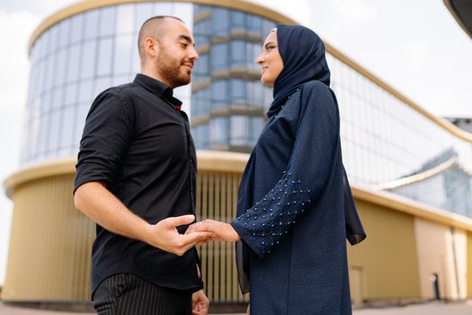 A couple holding hands in front of a glass building, symbolizing love and diversity.