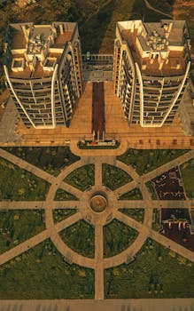 Aerial shot of twin residential buildings with landscaped park and playground at sunset.