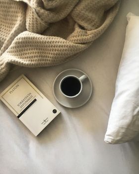 A peaceful morning scene with coffee, a book, and blanket on a bed, perfect for relaxation.