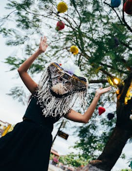 A woman celebrating outdoors with an elaborate mask under a tree adorned with colorful lanterns in Taiwan.