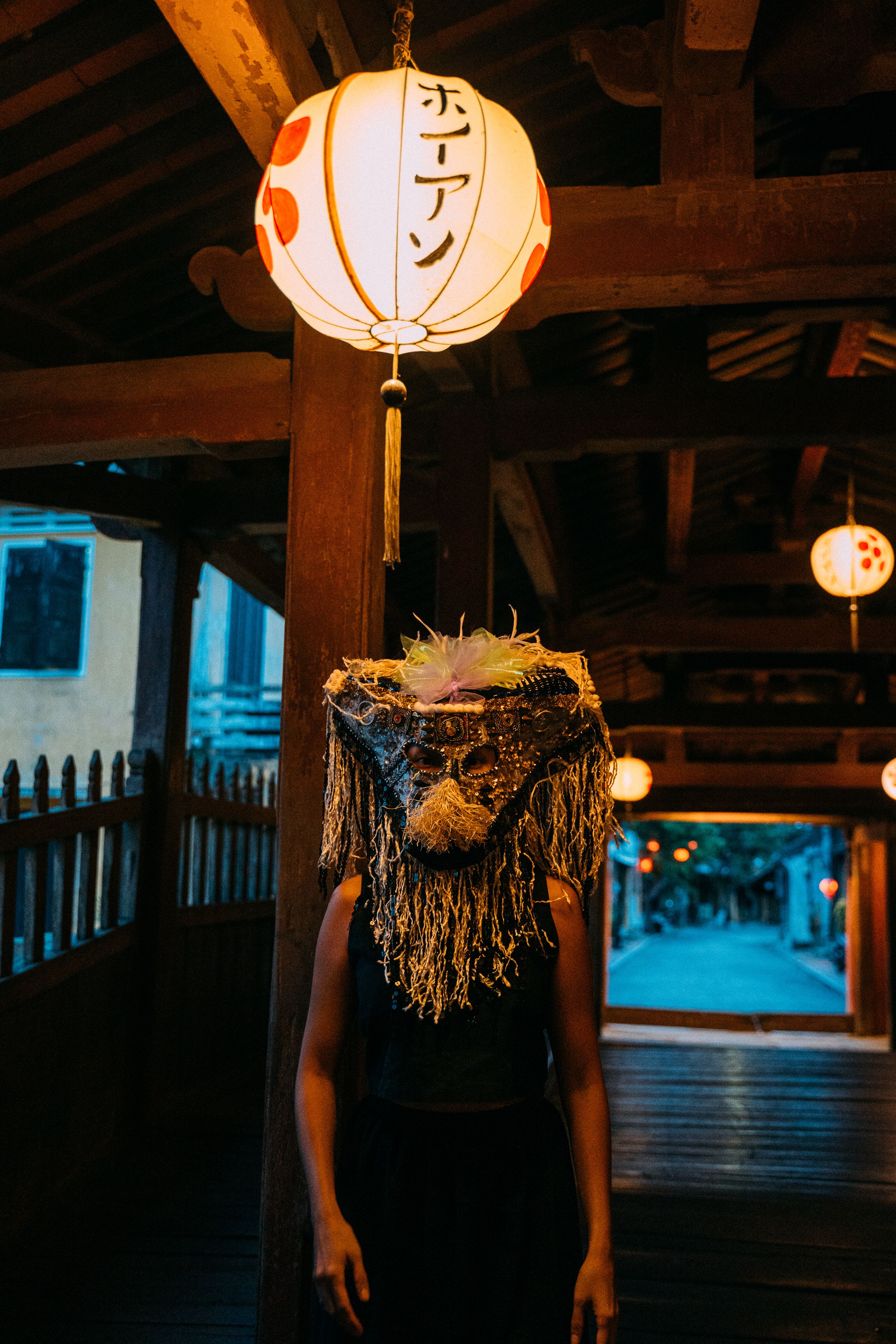 Mysterious figure in traditional mask stands under lantern in Taiwan's historic passageway.