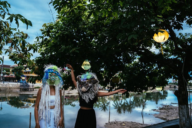 People In Ethnic Masks Standing By A Tree With Paper Lanterns