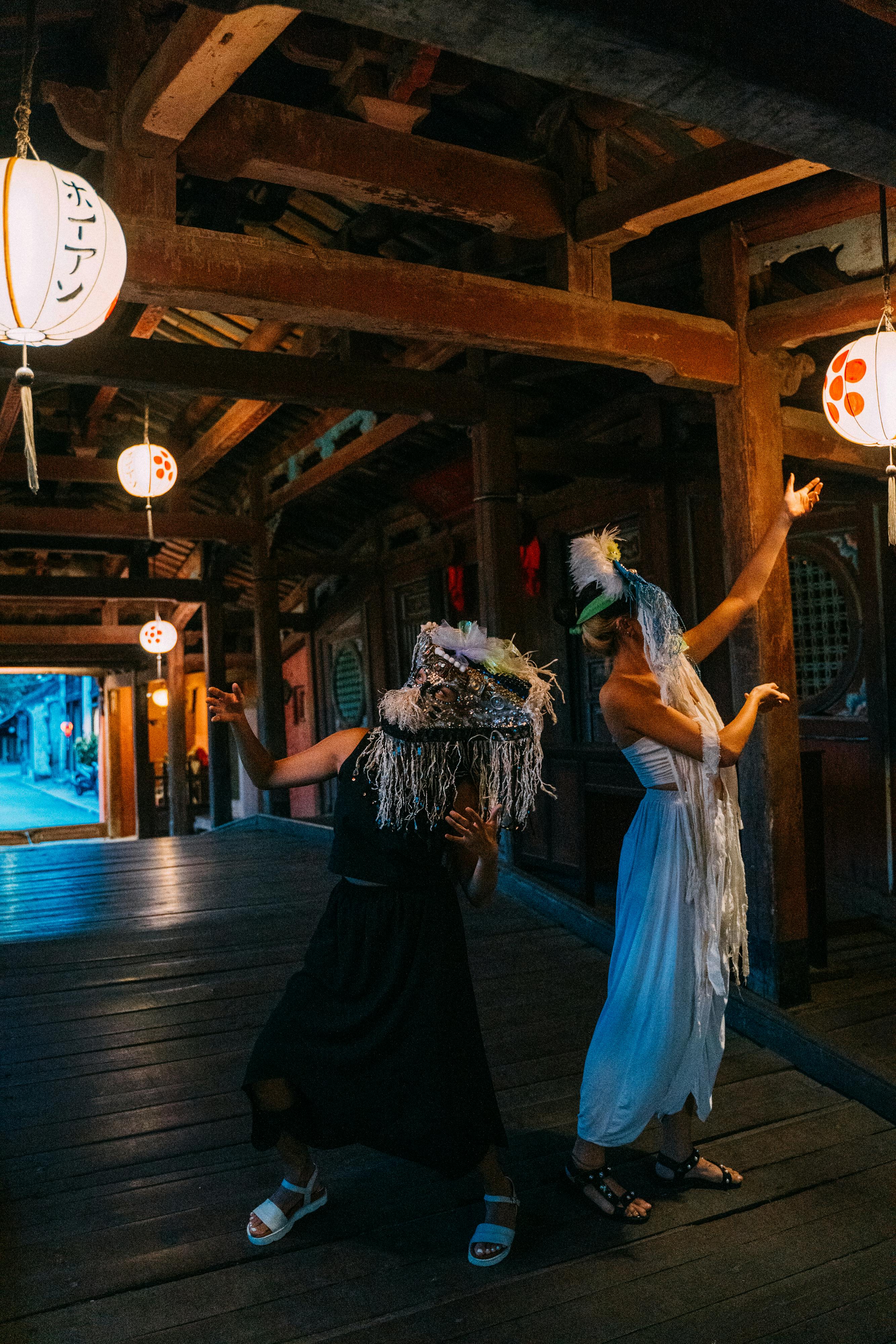 Free Two adults in elaborate masks and costumes pose on a lit wooden bridge, creating an ethereal ambiance. Stock Photo