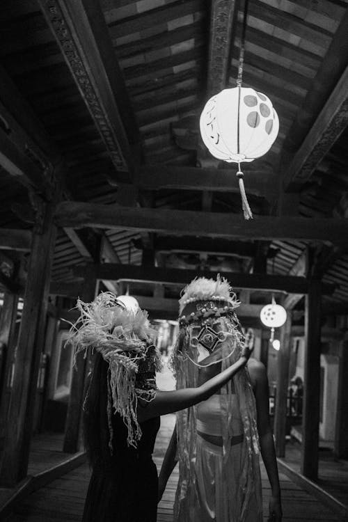 People in Ethnic Masks Doing Hand Gestures under a Paper Lantern