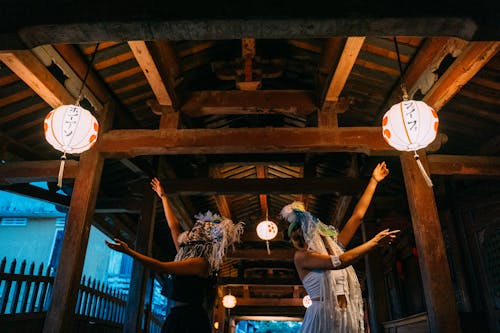 People in Ethnic Masks Doing Hand Gestures under Paper Lanterns