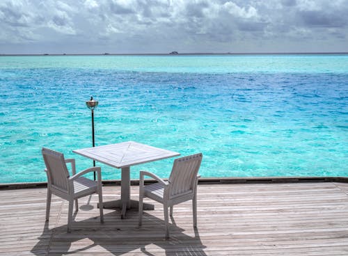 White Wooden Table and Chairs on Brown Wooden Dock Near Blue Sea