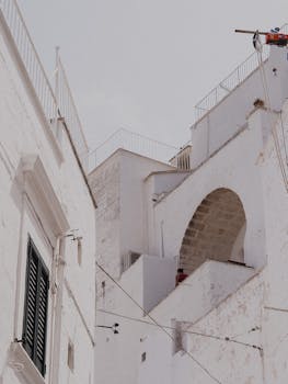 Low angle view of white stucco buildings with arches and railings under a clear sky.